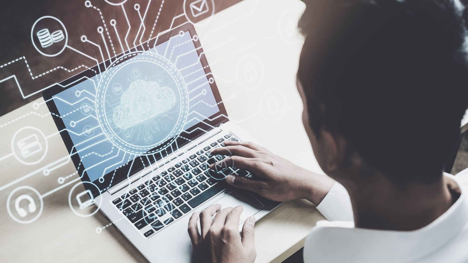 Home 6 Person working on a laptop with an illustrated cloud-computing interface displayed on the screen.